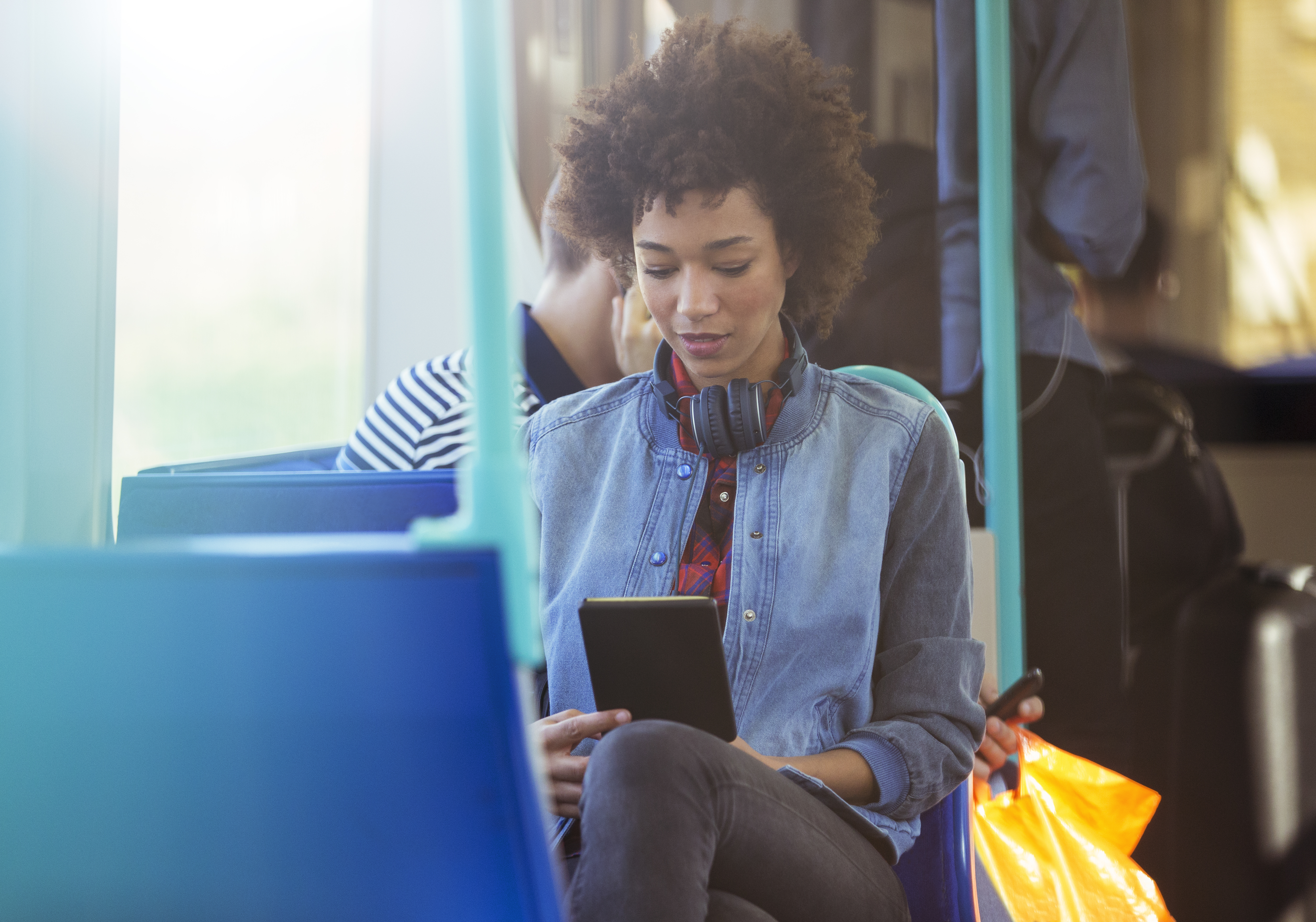 woman sitting on bus with headphones and tablet