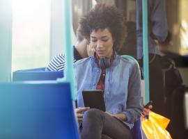 woman sitting on bus with headphones and tablet